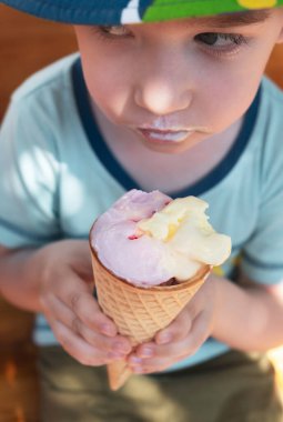 Güneşli yaz gününde dondurma yiyen bir çocuk. Yaz mevsiminde sıcak havada yemek ya da tatlı. Yakın, dikey