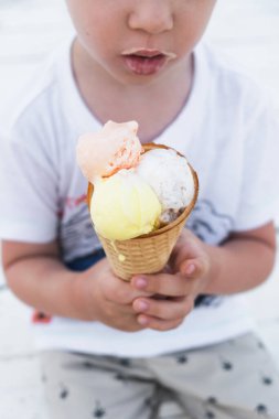 Güneşli yaz gününde elinde dondurma külahıyla küçük bir çocuk. Yaz mevsiminde sıcak havada yemek ya da tatlı. Yakın, dikey, seçici odaklanma