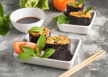 Çiğ rulo ve sebze dolgulu fesleğen ve gri arka planda soya sosu ile yosunlara sarılmış.