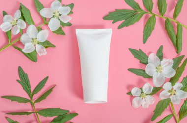 Sevgililer Günü hediyesi olarak kozmetik ürünleri, pembe arka planda yaprakları ve çiçek çerçevesi olan beyaz bir krem tüpü.