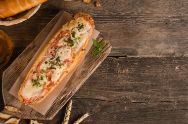 Ahşap zemin üzerinde peynirle ve domatesle doldurulmuş bir somun ekmek. Fotokopi alanı ve fast food içeriyor.