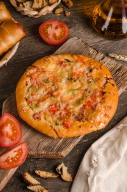 Peynirli ve domatesli pizza ahşap arka planda malzemelerle yakın plan.