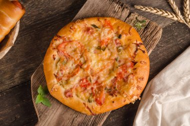 Peynirli ve domatesli pizza ahşap arka planda malzemelerle yakın plan.