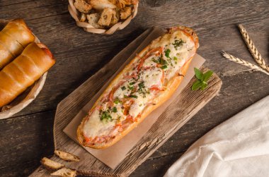 Ahşap bir zemin üzerinde peynirle ve domatesle doldurulmuş ekmek, malzemeler, fast food.