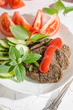 Çiğ sebze pirzolası ve sebzeli, soslu ve otlu mısır gevreği sert bir ışıkla beyaz bir tabakta yakın plan.