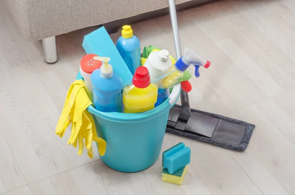 Various cleaning products with napkins, sponges and gloves in a blue bucket in the room. The concept of cleaning in the house, in the apartment.