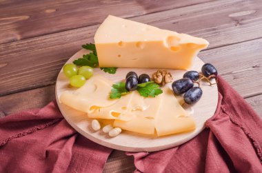 Taze dilimlenmiş sert peynir otlar ve üzümlerle süslenmiş koyu ahşap arka planda yuvarlak bir tahta üzerinde