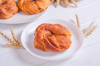 Beyaz tabakta beyaz ahşap arka planda taze tarçınlı şekerli çörek