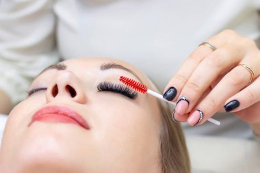 Kirpik uzatma prosedürü. Güzellik salonunda uzun kirpikleri olan güzel bir kadın. Kirpikleri kapat. ellerinizi fırçalayın.