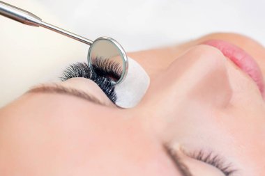 Kirpik uzatma prosedürü. Uzun kirpikli bir kadın gözü. Kapatın. Ayna ellerinde.