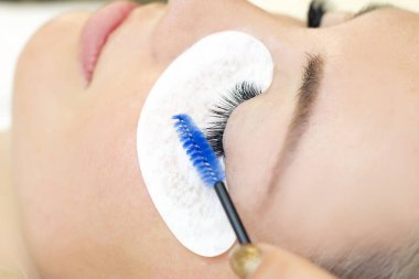 Kirpik uzatma prosedürü. Güzellik salonunda uzun kirpikleri olan güzel bir kadın. Kirpikleri kapat. ellerinizi fırçalayın.