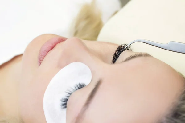 Eyelash extension procedure. Woman eye with long eyelashes. Close up. using tweezers