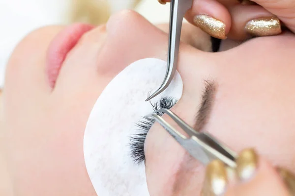 Eyelash extension procedure. Woman eye with long eyelashes. Close up. using tweezers