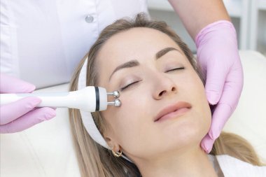 Donanım kozmetolojisi. Kapalı gözlü güzel genç bir kadının güzellik salonunda rf kaldırma prosedürü alırken yakın plan fotoğrafı..