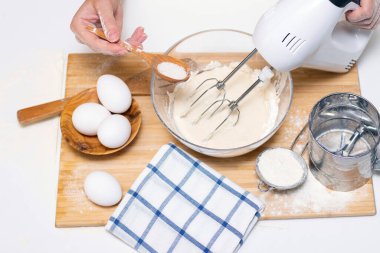 Ekmek ya da ev yapımı hamur işi yapmak. Malzemeler masanın üstünde. Kadın elleri hamuru karıştırmak için mikser tutuyor.