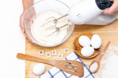 Kadın elleri hamuru karıştırmak için mikser tutuyor.