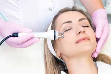 Donanım kozmetolojisi. Kapalı gözlü genç bir kadın güzellik salonunda RF kaldırma prosedürü uyguluyor..