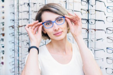Optik mağazasında gözlükçüyle yeni gözlük seçen genç bir kadın. Gözlükler optik mağazasında. Bir kadın gözlük seçer. Duygular. Oftalmoloji.