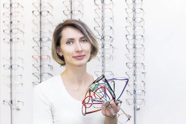 young woman in optic store choosing new glasses with optician. glasses in the store of optics. A woman chooses glasses. many glasses in hand. Ophthalmology.