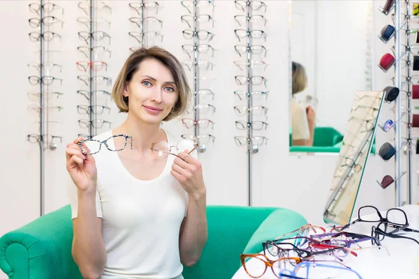 young woman in optic store choosing new glasses with optician. glasses in the store of optics. A woman chooses glasses. Emotions. Ophthalmology.