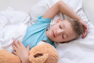 Çocuk tatlı tatlı uyuyor oyuncak ayıya sarılıyor