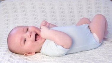 Bebek sırt üstü uzanıyor, gülüyor ve gülümsüyor, kameranın lensine bakıyor.