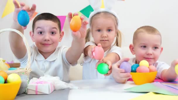 ウサギの耳の陽気な子供たちはイースターのために描かれた卵で遊んでいます 子供たちはお菓子と笑いを食べる 二人の男の子と女の子 — ストック動画