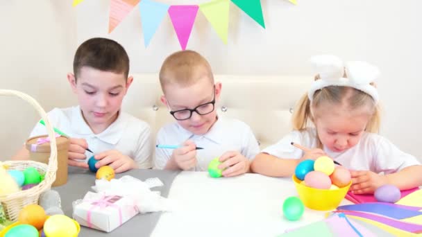 兔子耳朵里有趣的孩子们为复活节画鸡蛋 孩子们一边吃糖果一边笑 两个男孩和一个小女孩 — 图库视频影像