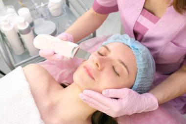 Kozmetik ofisinde genç bir kadının yüzünün ultrasonik temizlenmesi..