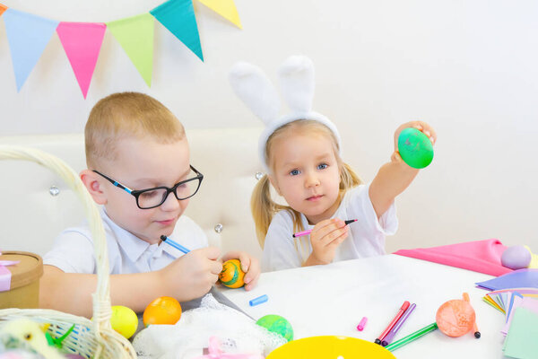 Забавные дети в кроличьих ушах рисуют яйца на Пасху. Дети едят сладости и смеются. мальчик и девочка
