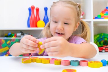 Konuşma terapisi, iyi motor becerilerin geliştirilmesi. Küçük kız ipte boncuklar sallıyor..