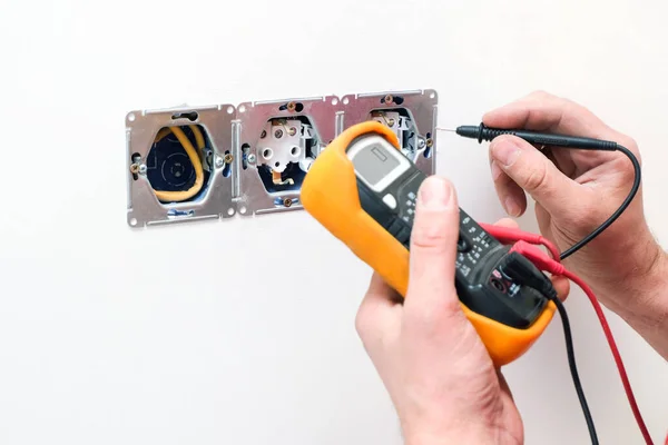 Electrician a wall socket with electronic multimeter. Wire and multimeter in hands close up