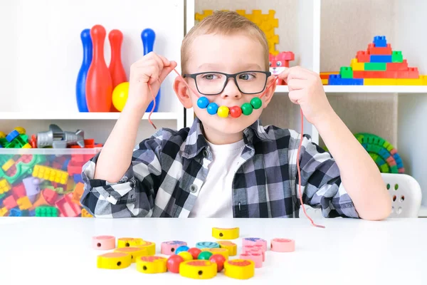 speech therapy, the development of fine motor skills. Toddler boy is stringing beads on a string. happy child