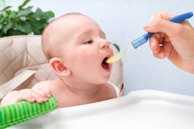 Bebeği besliyorum. Anne çocuğu bir kaşıkla sebze püresi ile besler. Yüksek bir sandalyede oturan mutlu çocuk