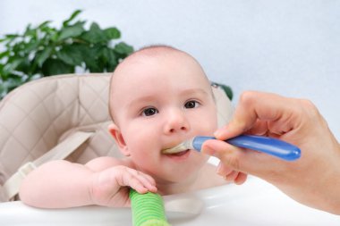 Bebeği besliyorum. Anne çocuğu bir kaşıkla sebze püresi ile besler. Yüksek bir sandalyede oturan mutlu çocuk