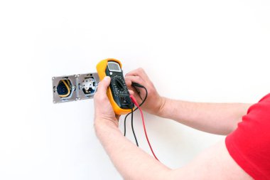 Elektrikçi. Elektronik çoklu sayacı olan bir priz. Kablo ve çoklu metre ellerinde.