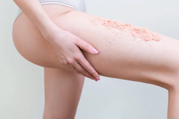 cropped view of young woman with scrub applying scrub to legs.