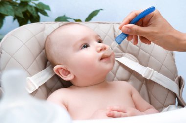 Bebeği besliyorum. Anne çocuğu bir kaşıkla sebze püresi ile besler. Yüksek bir sandalyede oturan mutlu çocuk