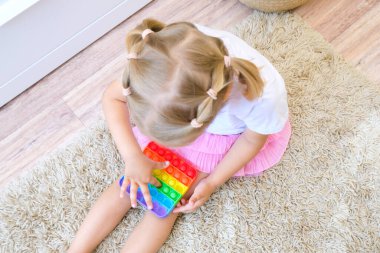 Tatlı suratsız çocuk Pop It 'le oynuyor. Popo kabarcığı esnek, duyusal oyuncağı itin, boşaltın ve çocuğun gelişmesine yardımcı olun.