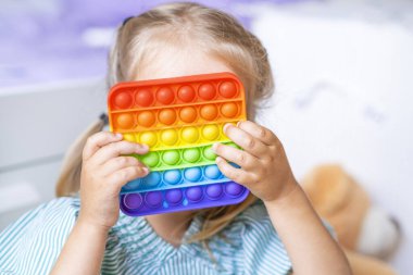 girl covers her face. The girl plays with the pop it sensory toy. Relief of stress and anxiety. Fashionable silicone game for stressed kids