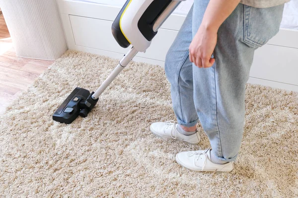 cordless vacuum cleaner is used to clean the carpet in the room. Housework with a new handheld vacuum cleaner. House cleaning, care and technology concept.