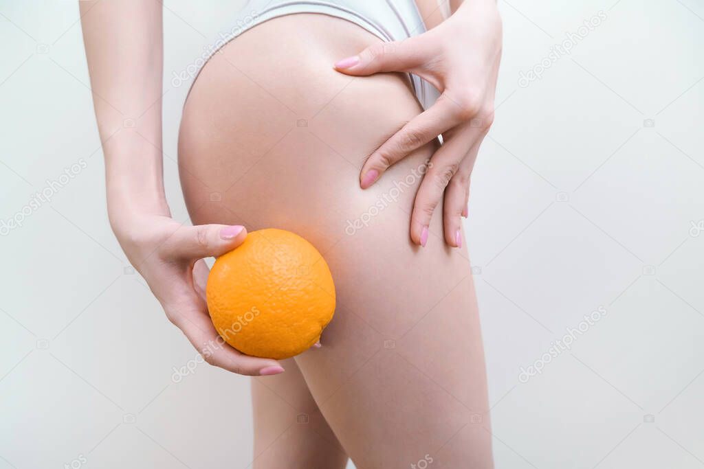 young woman is holding an orange on a light background. Cellulite problem concept