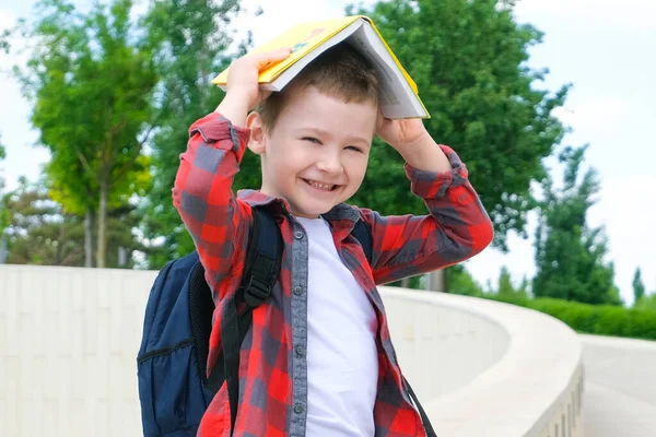 一个头上拿着一本书的小学生 就像在上学的路上的一个屋顶 回学校去 — 图库照片