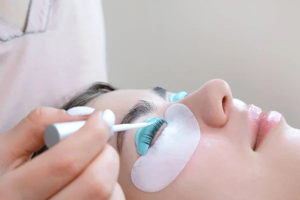 Young woman doing eyelash lamination procedure in a beauty salon, close-up