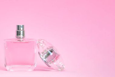 Pembe pastel arka planda açık kapaklı zarif bir parfüm şişesi.