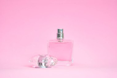 Pembe pastel arka planda açık kapaklı zarif bir parfüm şişesi.