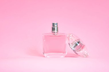 Pembe pastel arka planda açık kapaklı zarif bir parfüm şişesi.
