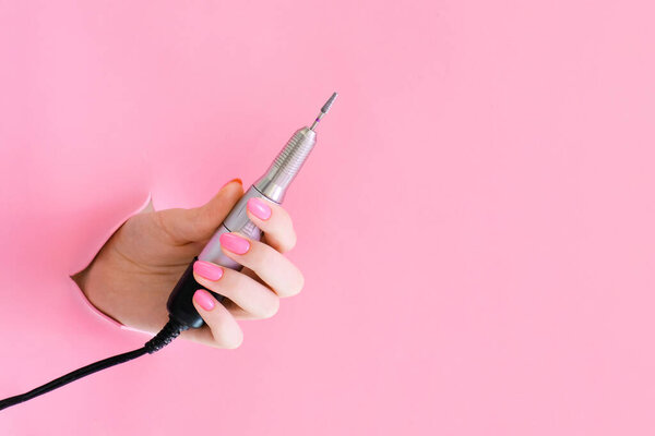 аппарат для маникюра в руке молодой женщины на розовом фоне из отверстия. Маникюр в твердой одежде. копировальное пространство