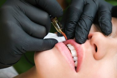 Güzellik salonunda dudaklarında kalıcı makyaj yapan genç bir kadın. Doğal yeşil arka plan. Kapat.