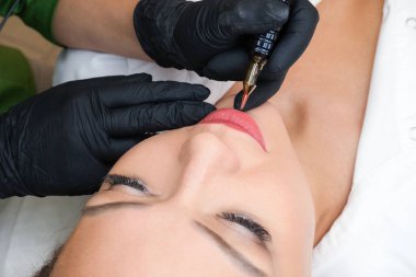 Güzellik salonunda dudaklarında kalıcı makyaj yapan genç bir kadın. Doğal yeşil arkaplan